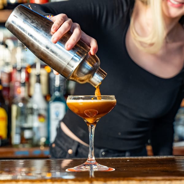 A bartender pours a dark amber cocktail from a shaker into a martini glass at One Station Plaza.