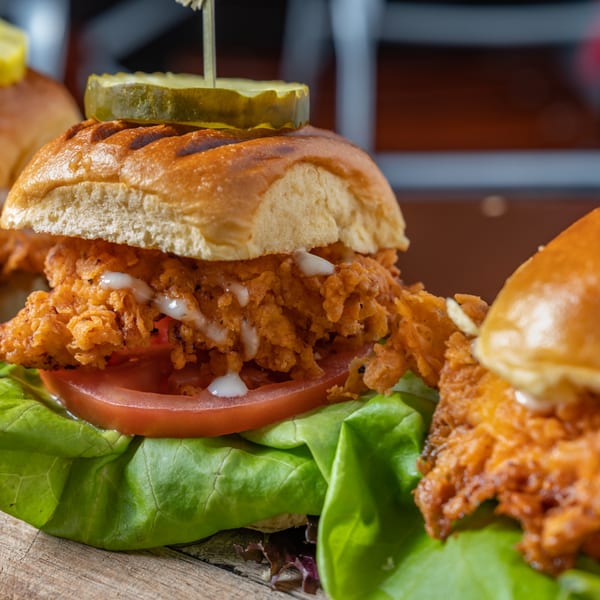 Close-up of a crispy fried chicken slider with lettuce, tomato, and a pickle on top.