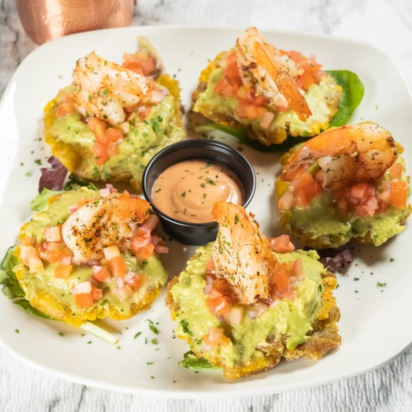Five shrimp tostones with guacamole, diced tomatoes, and a side of dipping sauce.