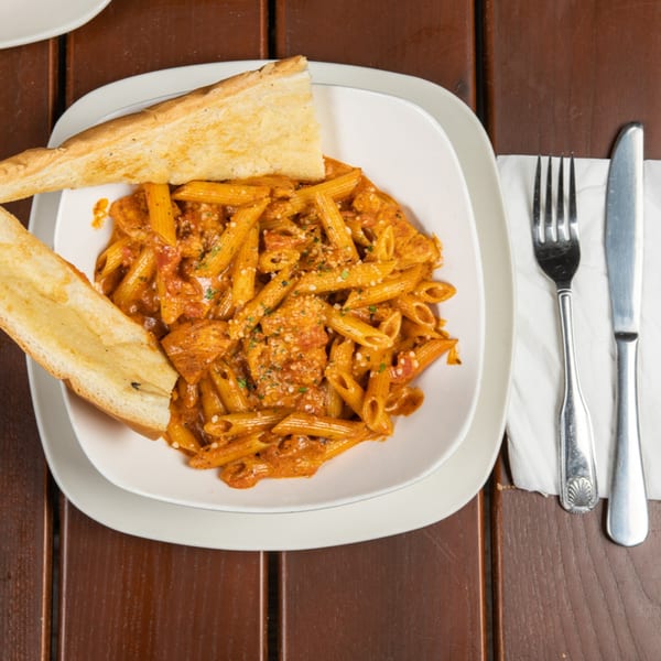 Penne pasta with creamy tomato sauce, chicken, and garlic bread on a wooden table.