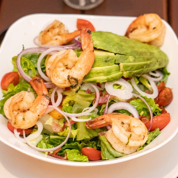 A vibrant American shrimp salad with avocado, red onions, tomatoes, and lettuce in a white bowl.