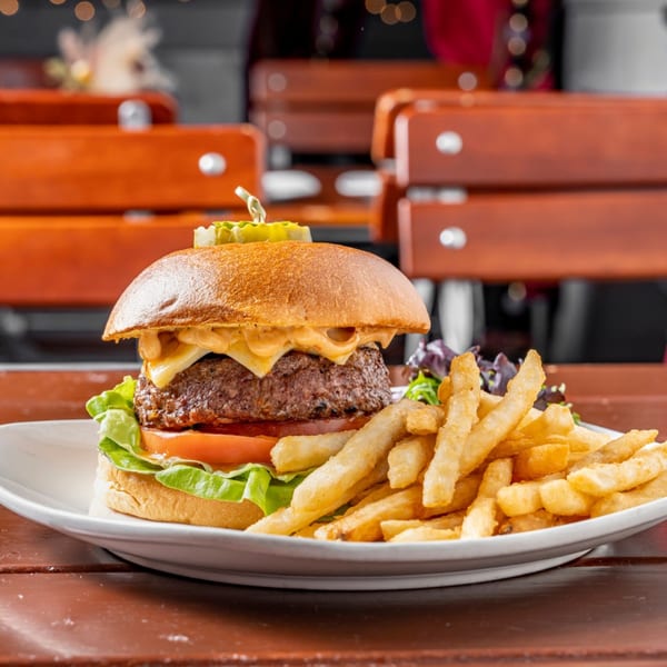 A juicy American burger with melted cheese, lettuce, tomato, and fries on a white plate.