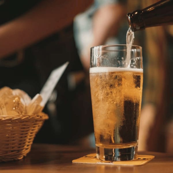Beer being poured from a bottle into a glass, with a bread basket in the background.