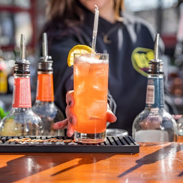 Bartender serving an orange cocktail with ice, a lemon slice, and a straw at One Station Plaza.