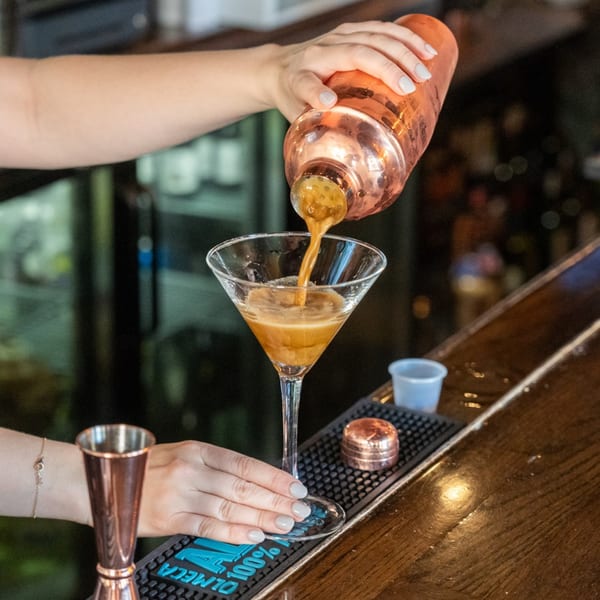 A bartender pouring a golden cocktail from a copper shaker into a martini glass at One Station Plaza.