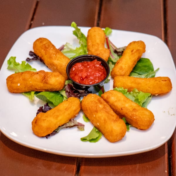 Golden-brown mozzarella sticks arranged in a circle with a cup of marinara sauce and lettuce.