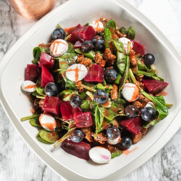 A vibrant beet and blueberry salad with goat cheese and candied walnuts in a white bowl.