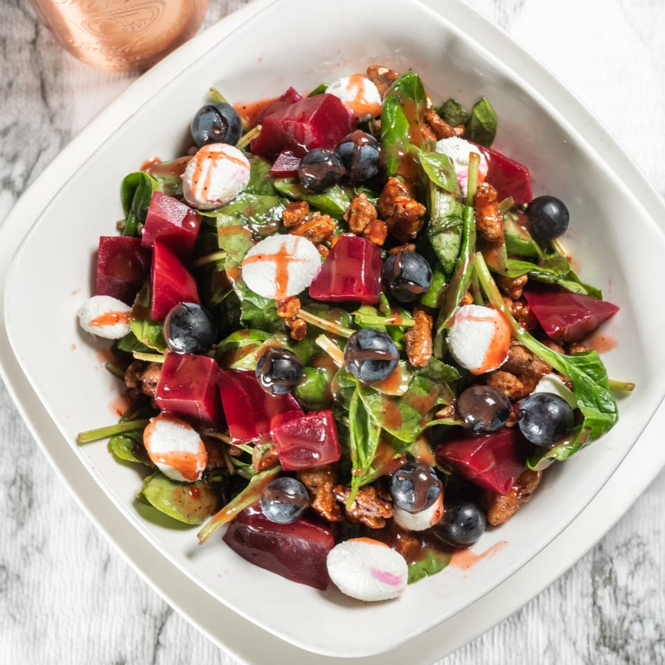 A vibrant beet and blueberry salad with goat cheese and candied walnuts in a white bowl.